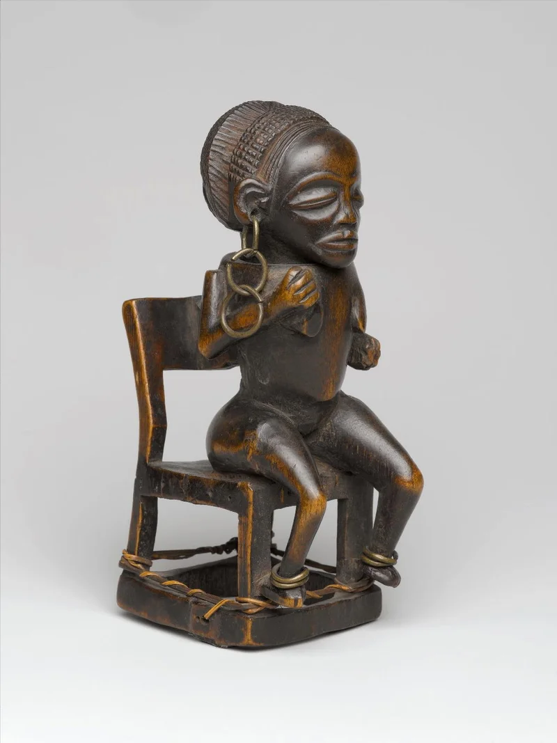 sculpture of a female figure sitting on a chair