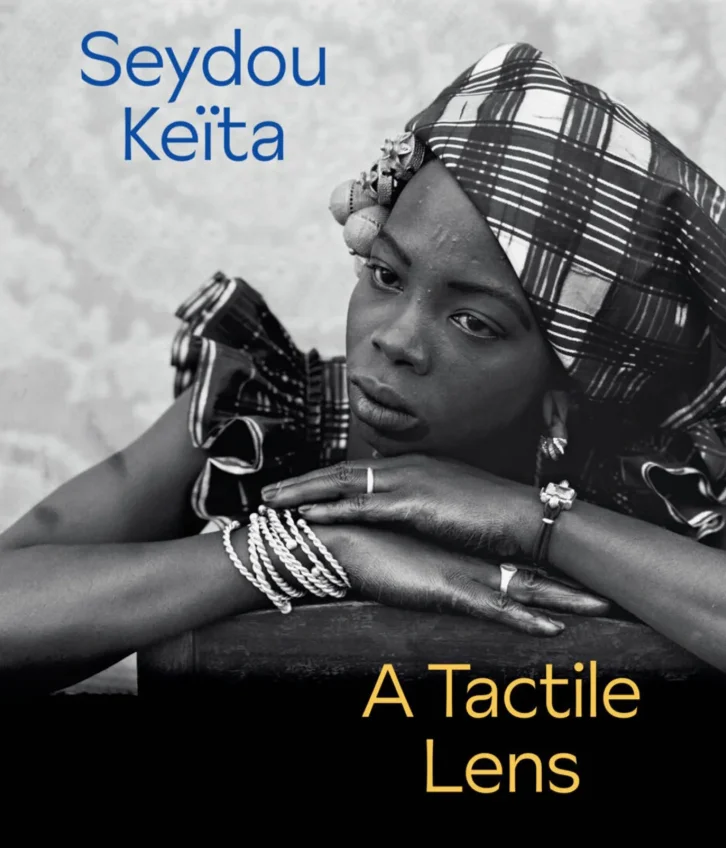 The cover of a catalogue depicting a woman posing with her hands under her face; the text reads "Seydou Keïta: A Tactile Lens"