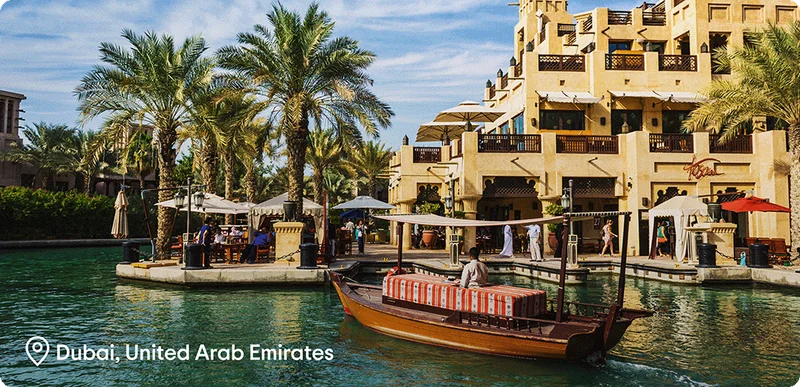 Image Description: A boat floating on a river with shops and palm trees in the background.