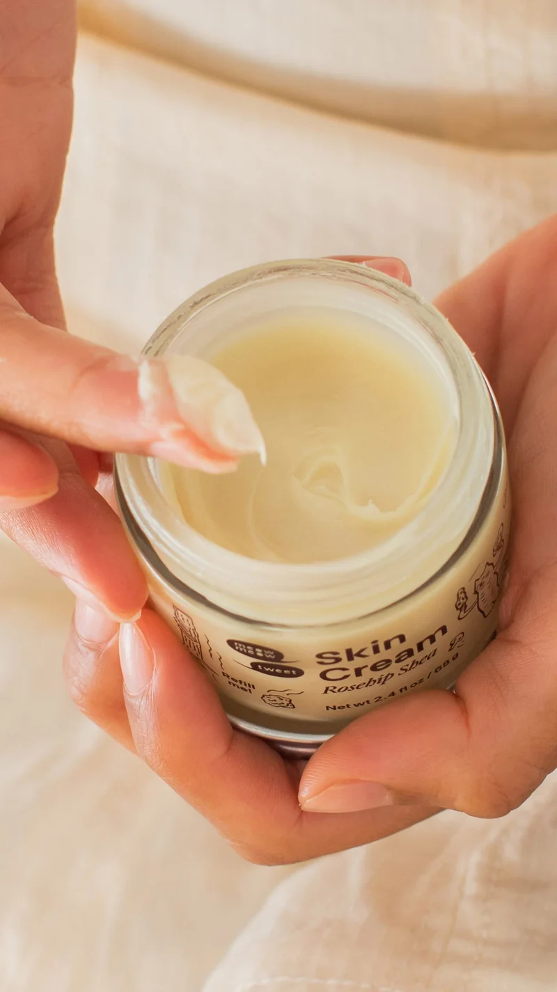 A tan jar of cream is shown in tall dried out grass