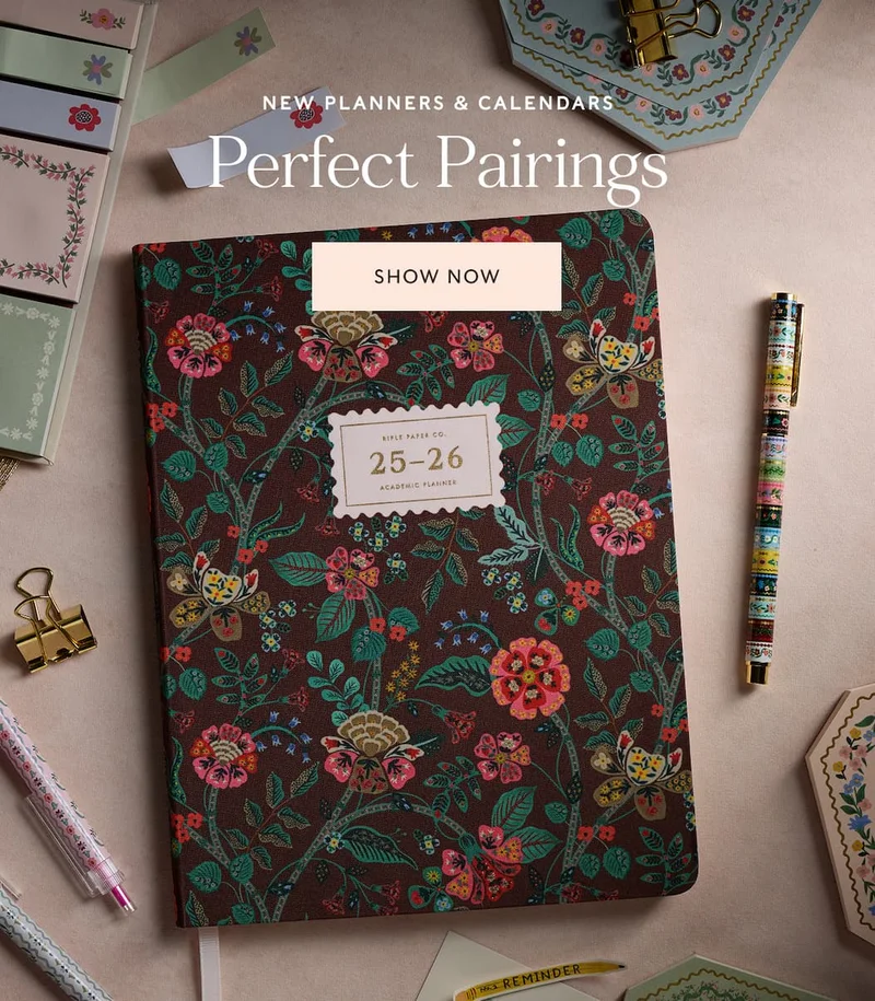 Floral 2025-2026 planner on desk with pens, clips, and accessories. Text reads "Perfect Pairing" and "Shop Now."