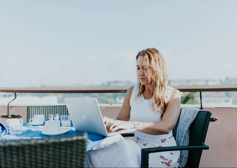 A woman sits on a patio working on a laptop.