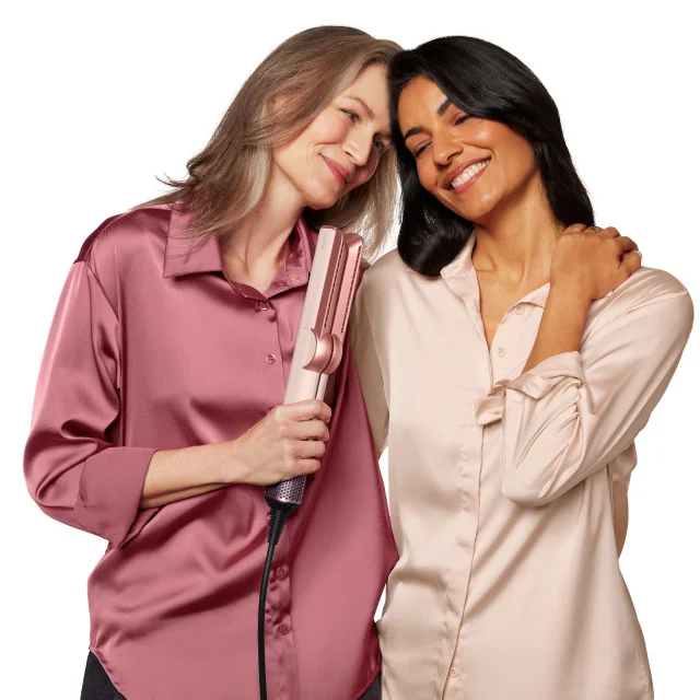 Two moms hugging while holding the Dyson Airstrait straightener in Ceramic pink and rose gold