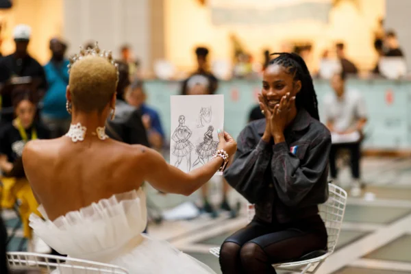 Two people facing each other; one of them holding a piece of paper with drawings on it