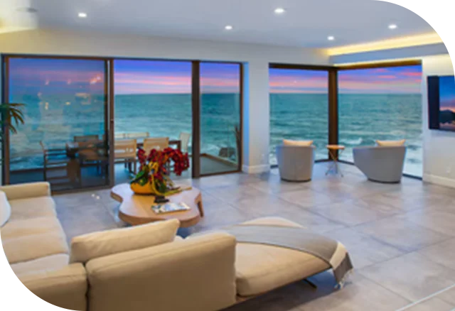 Modern beachfront living room with floor-to-ceiling windows overlooking the ocean at sunset.
