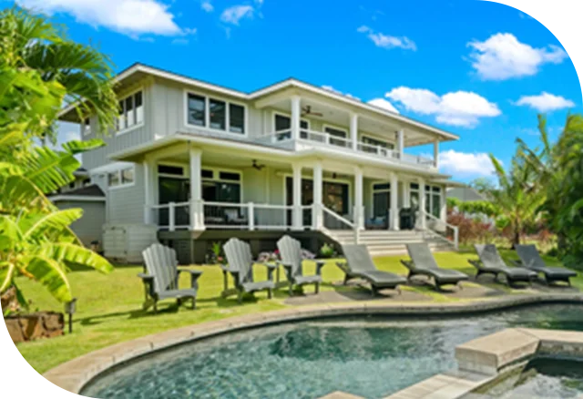 Two-story tropical home with wide porch, lawn chairs, and a curved pool under blue skies.