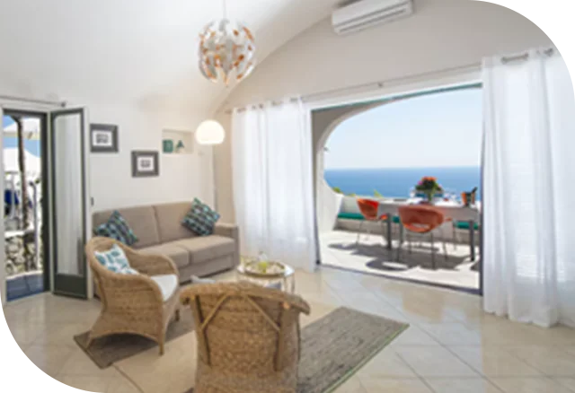 Bright coastal living room with wicker chairs and open terrace overlooking the sea.