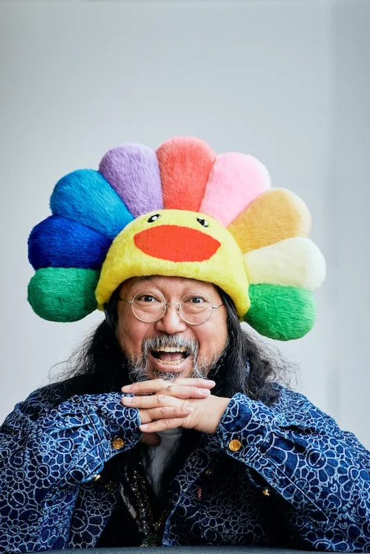 Photograph of Takashi Murakami smiling wearing a flower hat
