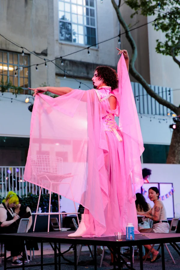 A photograph of an individual standing on a table wearing a flowing pink dress