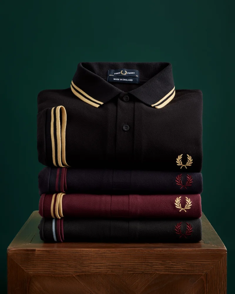 Made in England: four of our best-selling twin-tipped Made in England Fred Perry polo shirts are folded neatly and stacked on top of each other on a wooden plinth