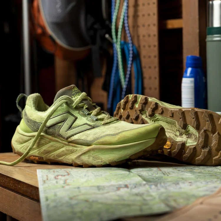 A pair of muddy, pale green New Balance sneakers sitting on a bench with a map.