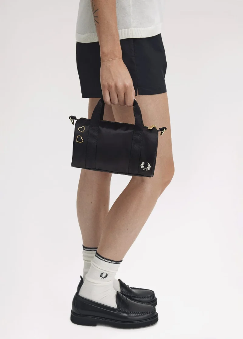 a cropped image of a female model's hand holding a mini black barrel bag from the Amy Winehouse collection