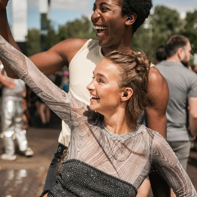 A man and woman dance at a sunny festival while wearing Loop earplugs.