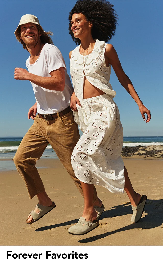 A man in Birkenstock sandals and a woman in Birkenstock clogs running on a beach.
