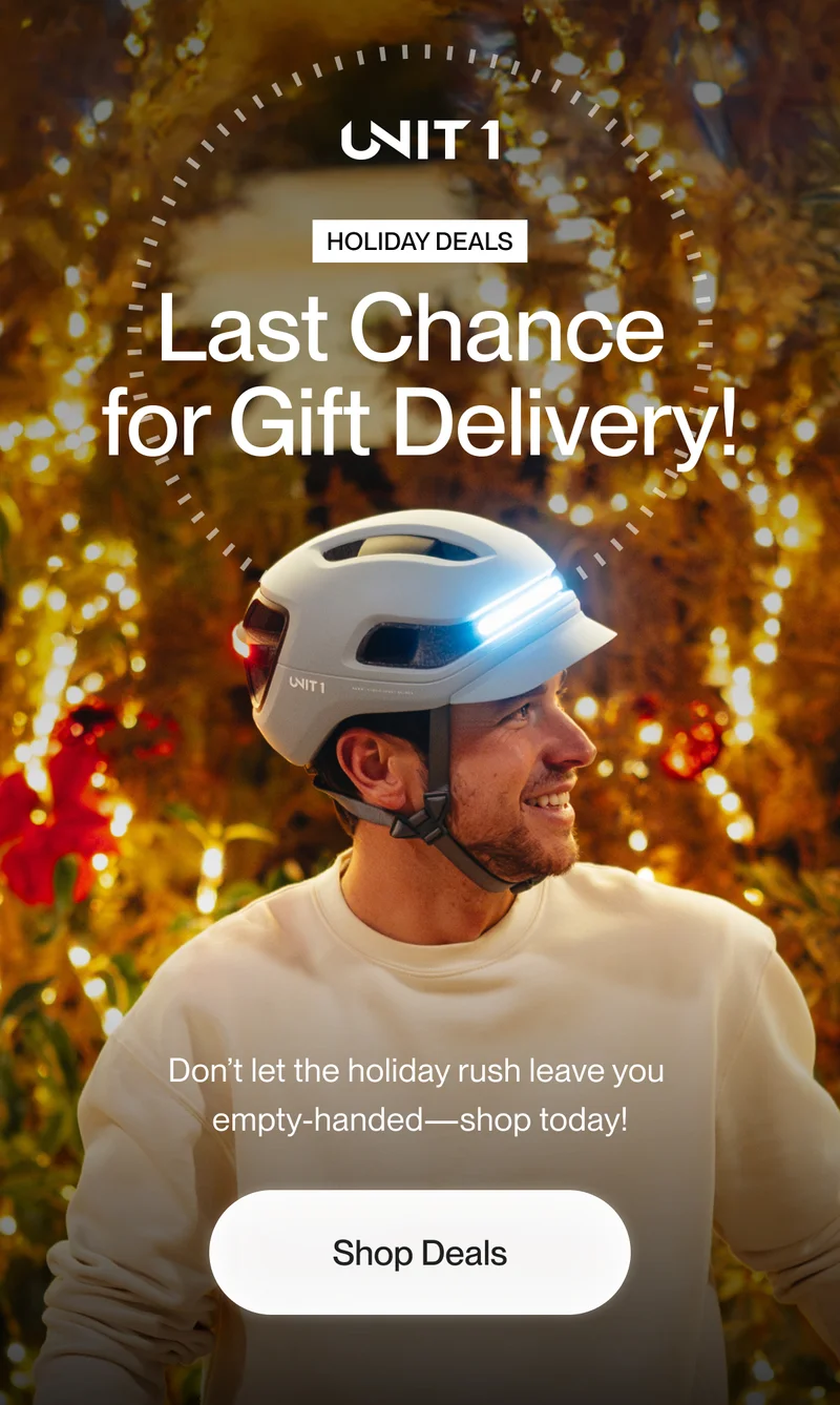 Cyclist wearing a smart helmet with glowing lights, smiling against a festive backdrop of holiday lights. Text reads 'Last Chance for Gift Delivery!' emphasizing the urgency of holiday shopping.