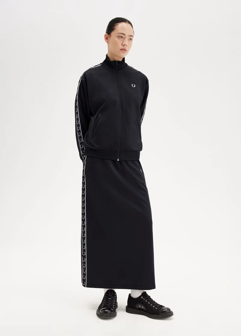 Asian female model with slick-back hair wears a full tracksuit; a black zipped jacket with monochrome taping and a matching ankle length skirt