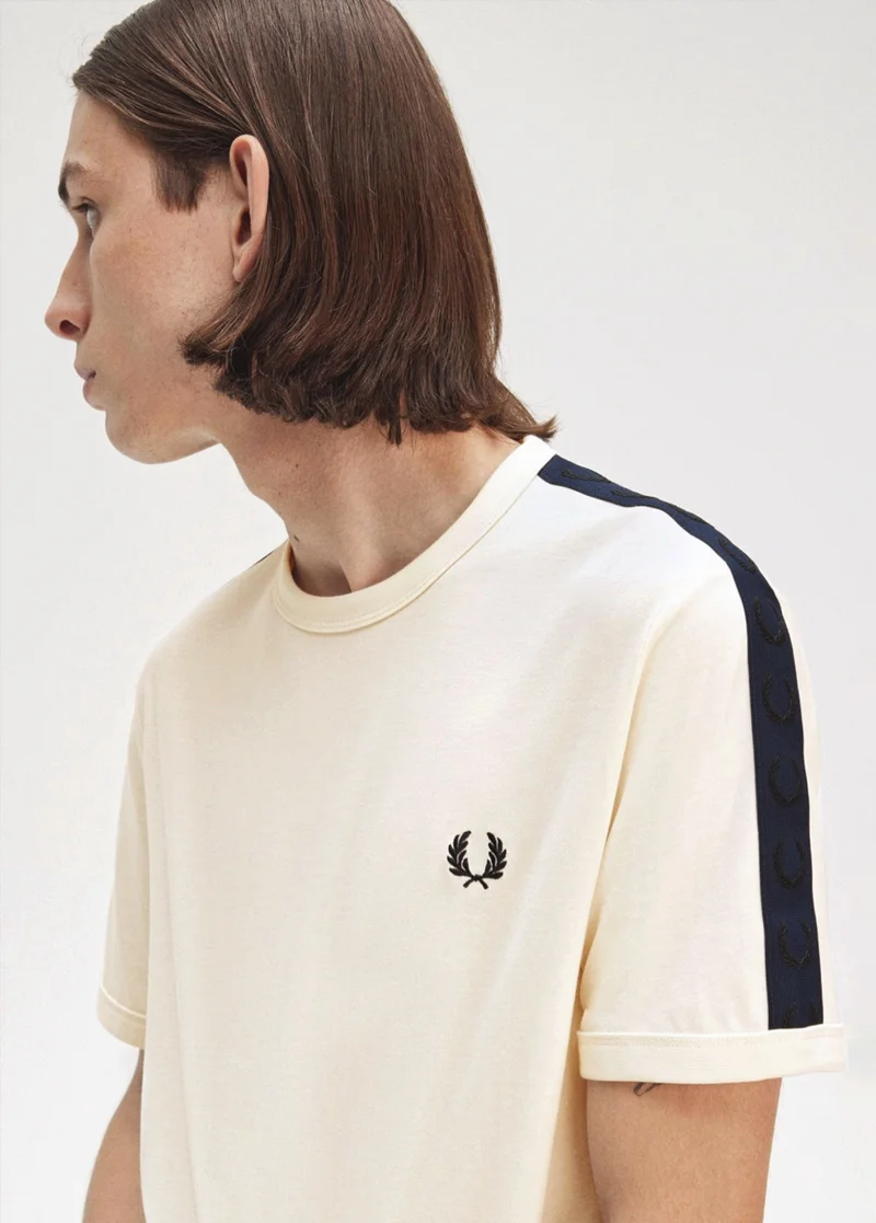 White male model with jaw-length brown hair wears ecru T-shirt with navy and black taping