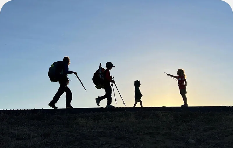 A silhouette of three children and an adult with hiking gear.