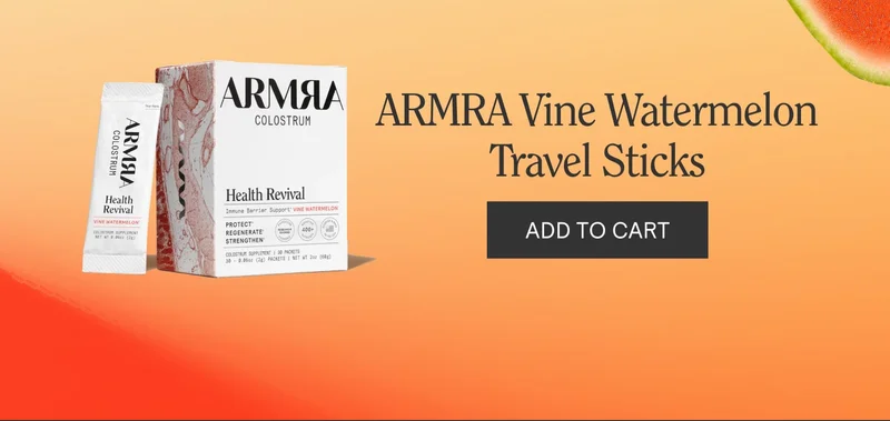 Box and stick packets of ARMRA Colostrum Health Revival Vine Watermelon flavor shown on a gradient orange background with watermelon slices and text reading ‘ARMRA Vine Watermelon Travel Sticks’ and an ‘ADD TO CART’ button.