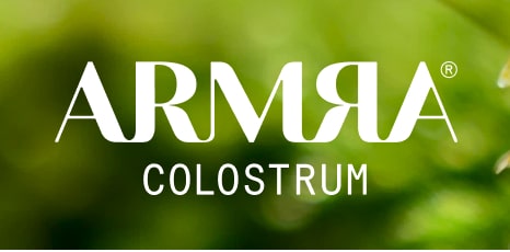 ARMRA Colostrum logo displayed in white text over a lush green blurred background.