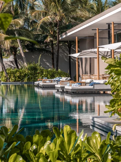 Over-water lounge seats with white umbrellas and palm trees.
