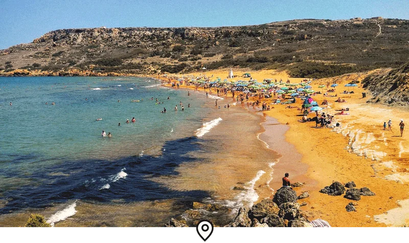 Image Description: Aerial view of travelers swimming and relaxing at Ramla Bay—a remote beach with orange sand, surrounded by rocky mountains