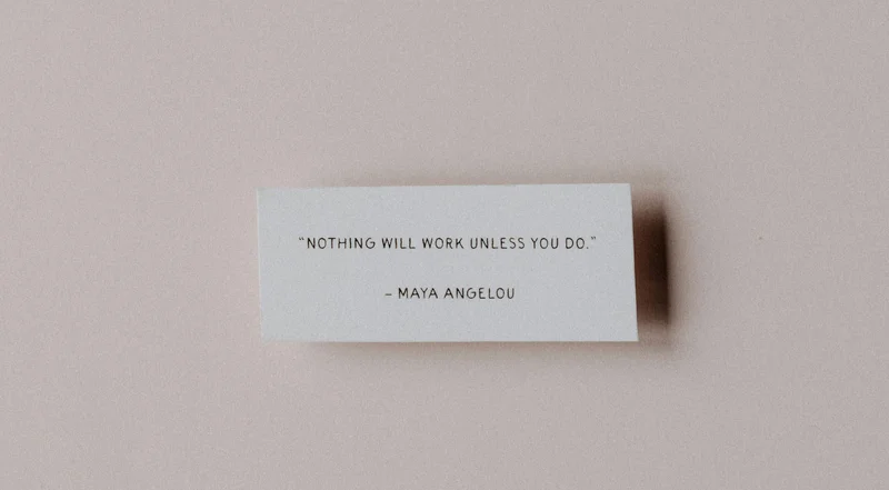 A white piece of paper on a pale pink background with a quote by Maya Angelou that reads, “Nothing will work unless you do.”
