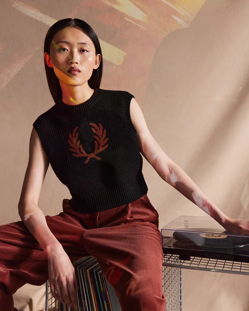 Woman wearing whisky brown corduroy trousers and a black knitted vest with a whisky brown laurel wreath
