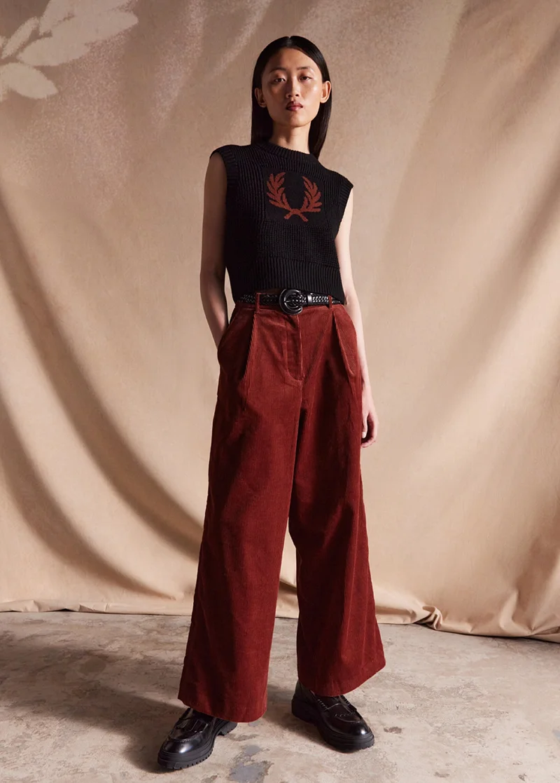 Woman wearing whisky brown corduroy trousers and a black knitted vest with a whisky brown laurel wreath