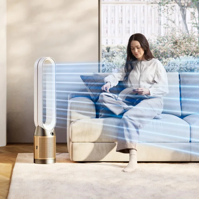 A woman sitting on a sofa reading while a Dyson purifier cleans the air