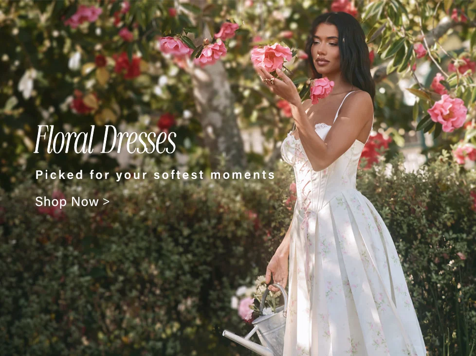 Elegant woman in a cream floral dress with pink rose patterns, holding a flower in a beautiful garden. Explore floral dresses for your softest moments.