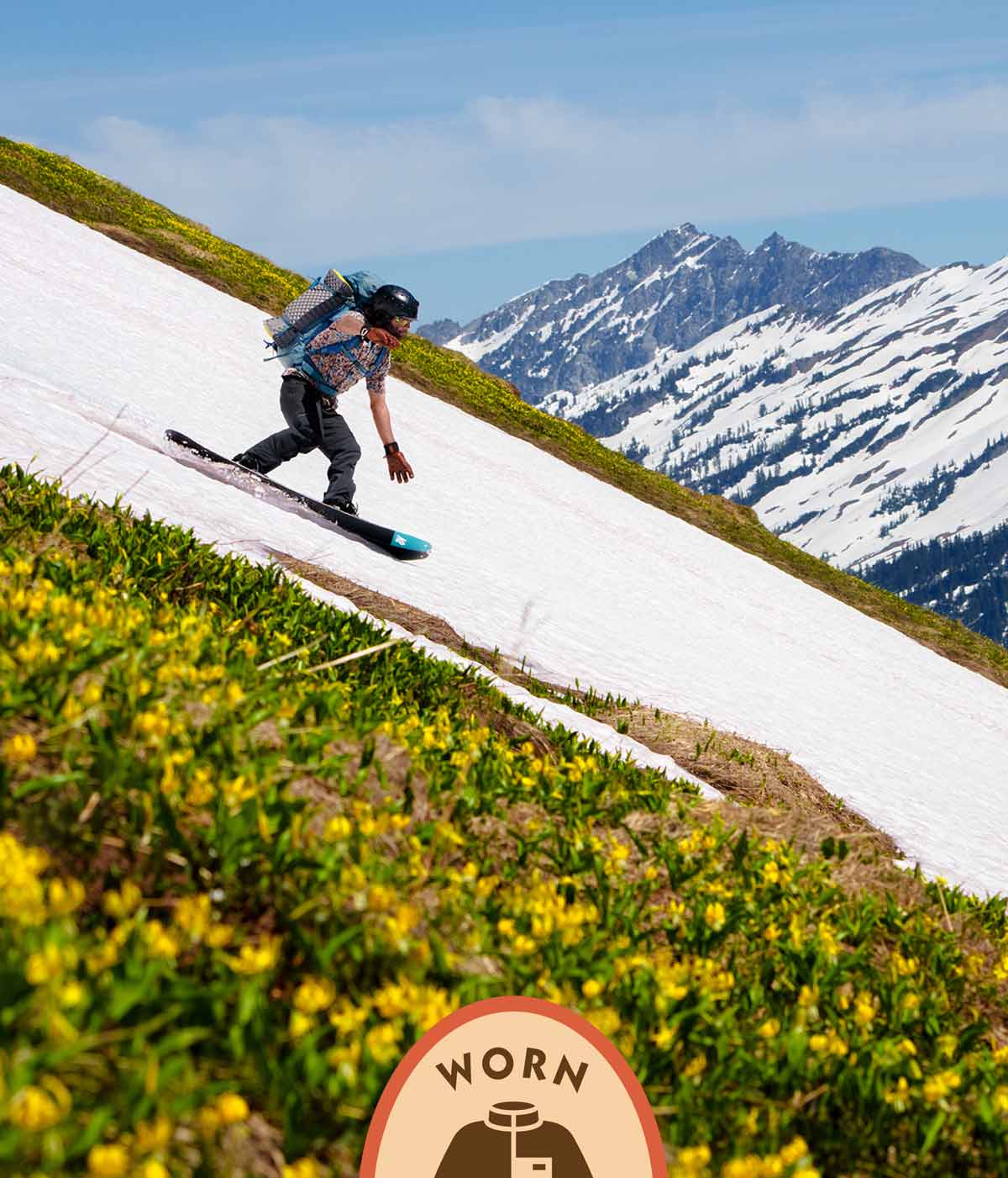 Patagonia Worn Wear. A person snowboarding on a patch of snow running through flowers.