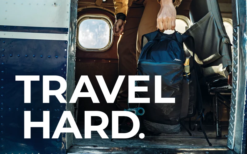 Man pulling backpack onto small plane: Travel Hard.