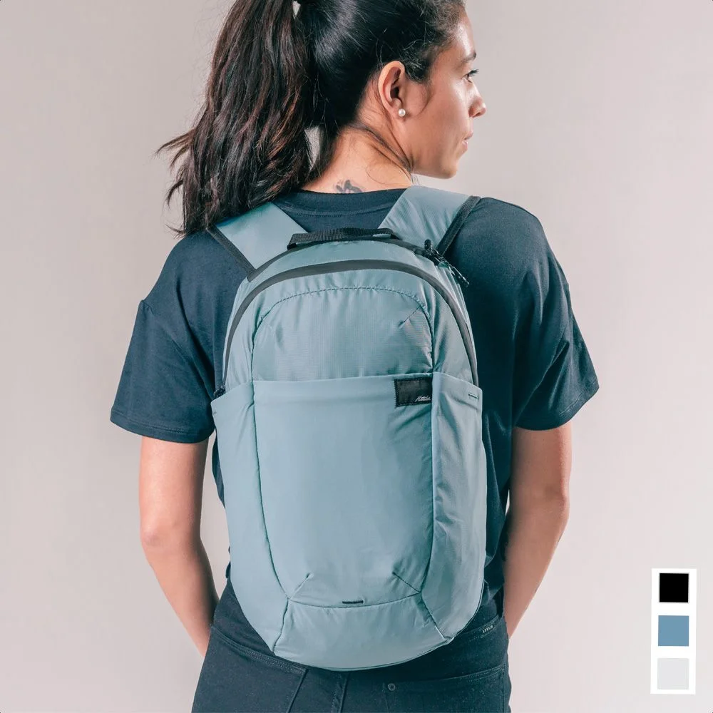 Back view of woman wearing a light blue backpack on warm grey background