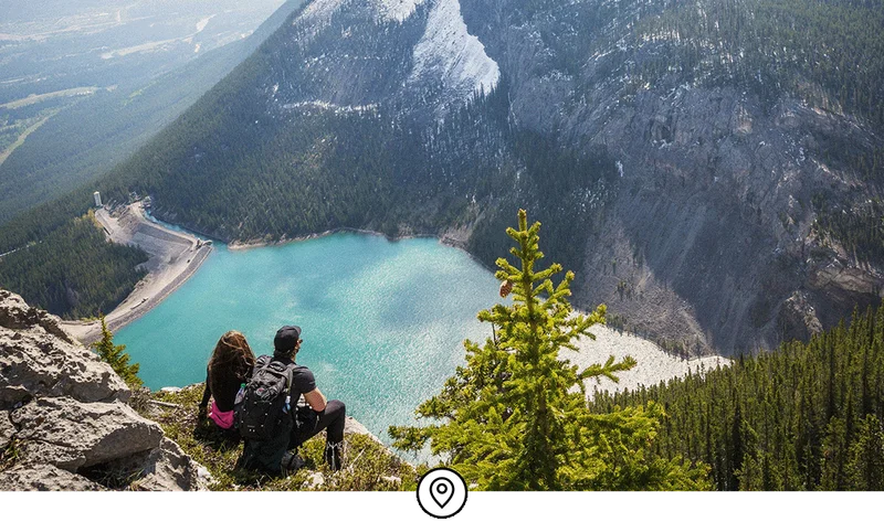 Image Description: Two people sitting on a mountain overlooking a lake.