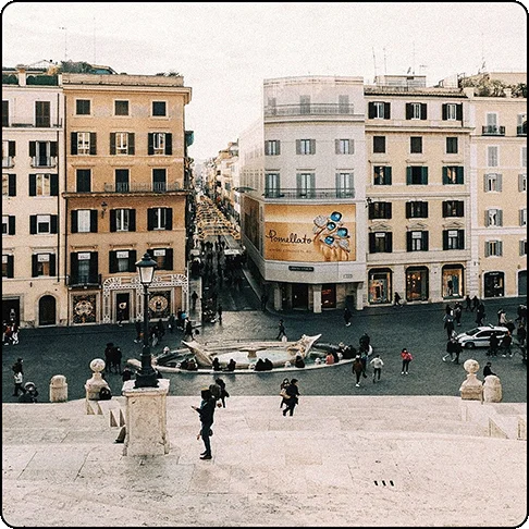 Image Description: Open plaza with large fountain in the center and marble steps. Old European-style buildings in the background.