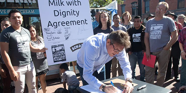 Former Ben & Jerry's CEO Jostein Solheim signs the Milk With Dignity agreement with Migrant Justice in October 2017 while Migrant Justice activists look on.