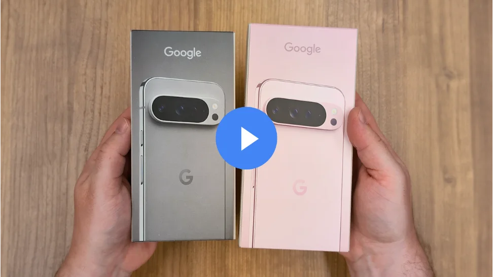 Two Google Pixel phone boxes are held side-by-side. The left box is gray and contains a Pixel 9 Pro. The right box is pink and contains a Pixel 9 Pro XL.