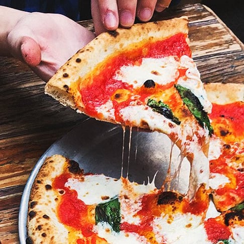Image Description: A traveler grabbing a slice of fresh Pizza Margherita