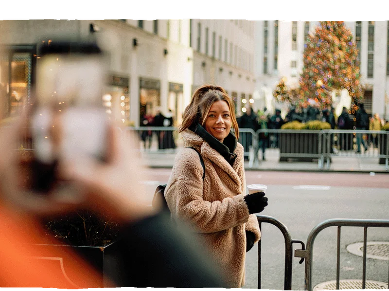 Image Description: A traveler posing for a photo with a Christmas tree in the background in New York City