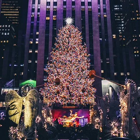 Image Description: A brightly-lit Christmas tree in front of Rockefeller Center