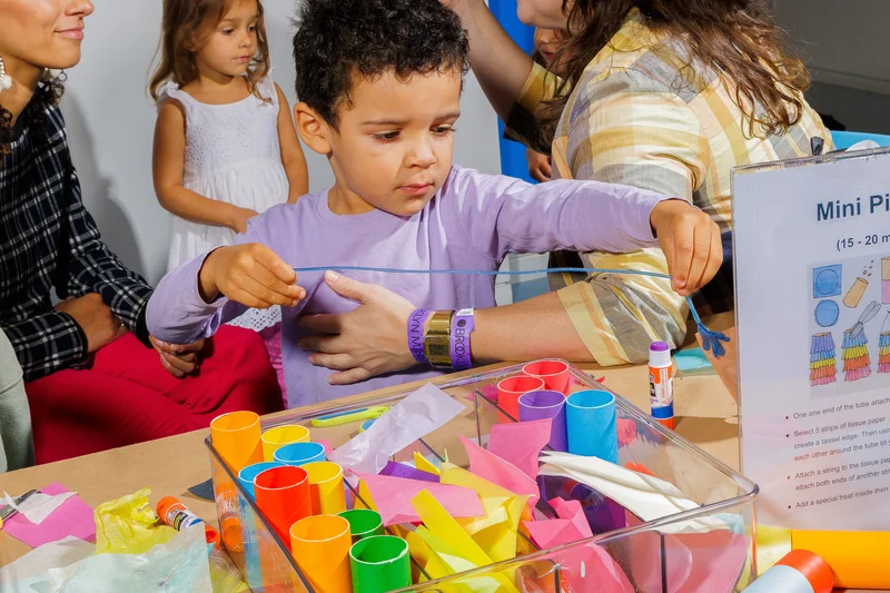 A kid makes art with colorful paper and glue sticks