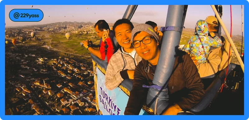 Image description: Two travelers smiling for a picture in a hot air balloon, photo taken by @229yass