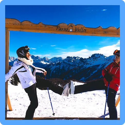 Image description: Two travelers with ski poles and helmets touching their ski boots together on a mountain