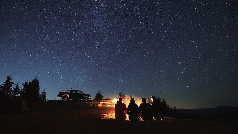 Image description: Hikers sitting near a campfire under a starry sky.