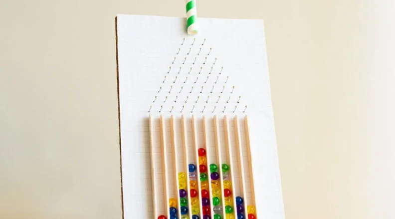 Image of a wooden pegboard with colorful beads forming a bell curve pattern as they fall through a triangular array of pegs.