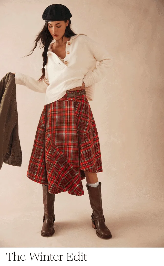 Alt text: A woman wearing a sweater, plaid skirt, boots and hat.