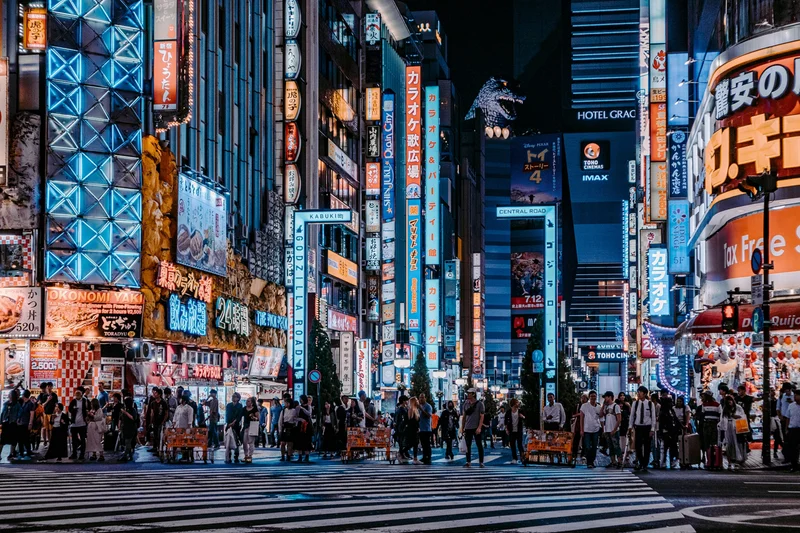 People standing at a crossing in a city centre surrounded by skyscrapers and neon lights