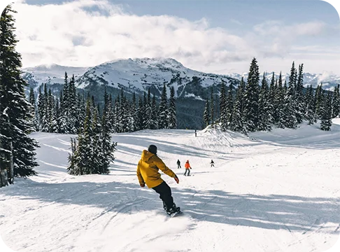 Image Description: A person snowboarding with trees and mountains in the background.