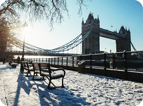 Image Description: Two benches in the snow near a bridge.